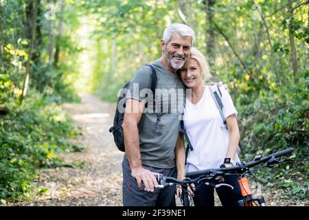 Portrait d'un couple mûr souriant avec des vélos debout sur un sentier en forêt Banque D'Images