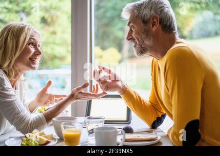 Un couple d'âge mûr souriant parle les uns avec les autres tout en prenant le petit déjeuner Banque D'Images