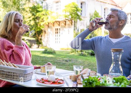 Couple d'âge mûr qui boit du vin rouge tout en étant assis à table Banque D'Images