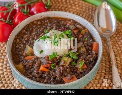 Ragoût avec des lentilles de béluga, des légumes et de la crème aigre servis dans un bol d'en haut avec une cuillère Banque D'Images