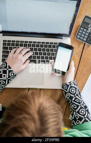 Vue de dessus d'une femme utilisant un smartphone tout en travaillant sur un ordinateur portable Banque D'Images