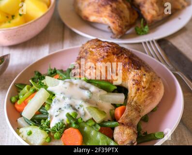 Des cuisses de poulet grillées avec des légumes, des pommes de terre et de la sauce sur une assiette de dessus sur une table de cuisine Banque D'Images