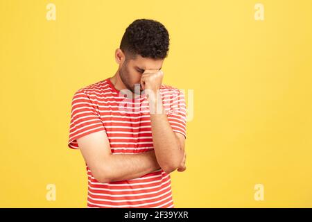 Un homme désespéré dans un t-shirt rayé abaissant sa tête cacher les yeux, contrarié déprimé à propos de l'erreur, se casse, sentiment de honte. Studio intérieur sho Banque D'Images