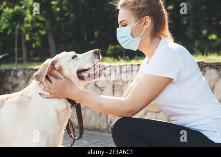 La femme blonde portant un masque médical joue avec son or retriever lors d'une promenade dans le parc Banque D'Images