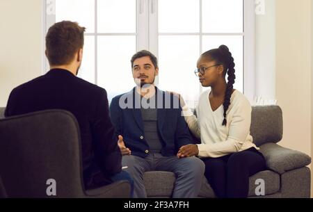 Jeunes conjoints interraciaux qui parlent à un spécialiste de l'homme lors d'une consultation familiale Banque D'Images