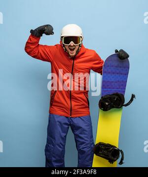 Snowboarder masculin en costume de ski brillant avec surf des neiges isolé sur fond bleu. Banque D'Images