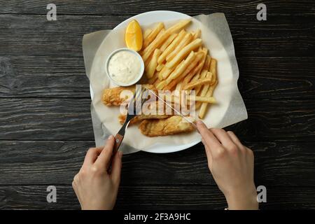 Femme mangeant du poisson frit et des frites sur fond de bois, vue de dessus Banque D'Images