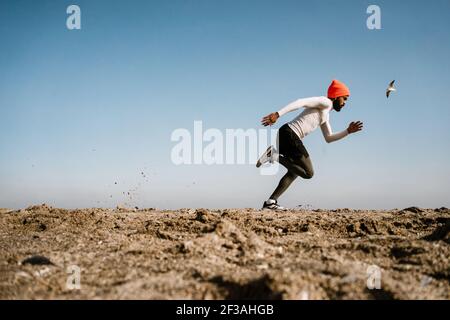 Sportif afro-américain sportif en écouteurs lors de l'entraînement à la plage Banque D'Images