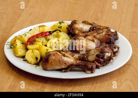 Pilons de poulet cuits avec des pommes de terre cuites, arrosées d'aneth et décorées de piment chaud mariné.Tout est servi sur une pl blanche Banque D'Images