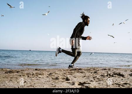 Sportif afro-américain sportif en écouteurs lors de l'entraînement à la plage Banque D'Images