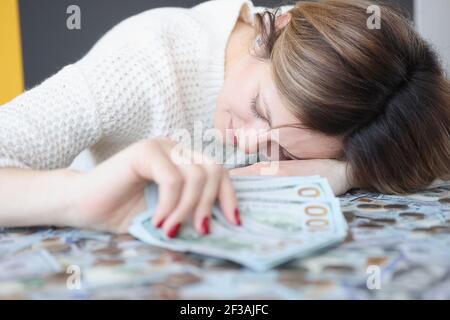 Jeune femme couché sur un tas d'argent et tenant des dollars entre ses mains Banque D'Images