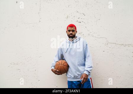 Homme afro-américain confiant dans des écouteurs debout avec le basket-ball en plein air Banque D'Images