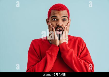 Un homme afro-américain choqué exprime sa surprise face à un appareil photo isolé arrière-plan bleu Banque D'Images