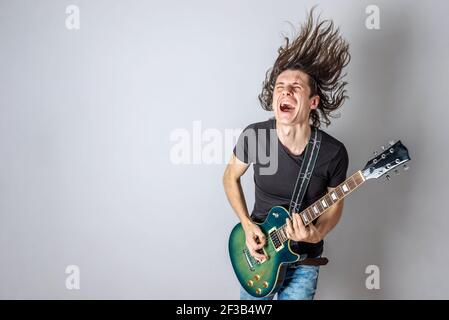 Un jeune homme joue une guitare électrique en chantant et en agitant ses cheveux longs. Performances émotionnelles du rock and roll Banque D'Images