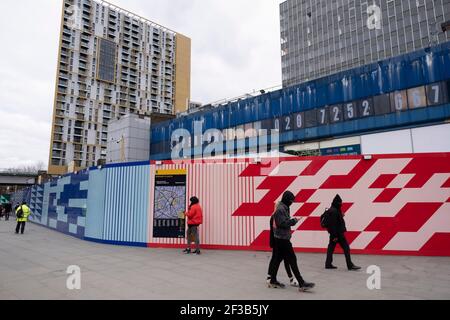 Les gens passent devant une palissade qui entoure le centre commercial Elephant and Castle, actuellement fermé, qui doit être démoli le 5 mars 2021 à Londres, au Royaume-Uni. La zone est maintenant soumise à un plan directeur de réaménagement budgétisé à 1.5 milliards de livres sterling. Un cadre de développement a été approuvé par le Conseil Southwark en 2004. Il couvre 170 acres et envisage de restaurer l'éléphant au rôle de centre urbain majeur pour le sud de Londres. Banque D'Images