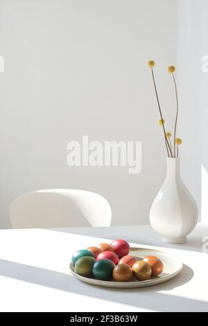 Œuf dur coloré sur une assiette en faïence de couleur jaune fleurs séchées dans un vase blanc en céramique dans un blanc espace Banque D'Images
