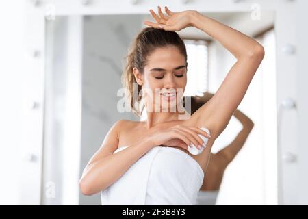 Femme appliquant les aisselles anti-transpiration de Deodorant pour la protection de la sueur dans la salle de bains Banque D'Images