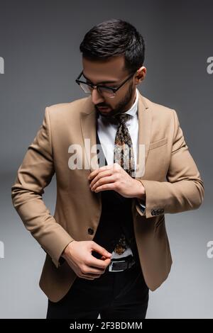 jeune homme arabe dans des vêtements tendance touchant blazer sur gris Banque D'Images