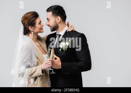 bonne mariée avec coupe de champagne embrassant le cou de l'élégant arabe homme isolé sur gris Banque D'Images