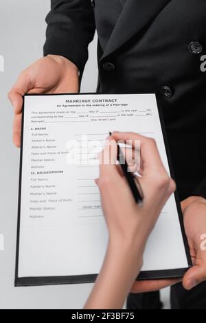 Vue rognée du marié tenant contrat de mariage près de la mariée avec stylo isolé sur gris Banque D'Images