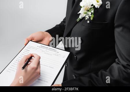 Vue rognée du marié tenant contrat de mariage près de la mariée avec stylo isolé sur gris Banque D'Images