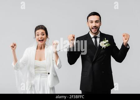 Mariée interraciale excitée et marié dans les menottes montrant ouais isolé en gris Banque D'Images
