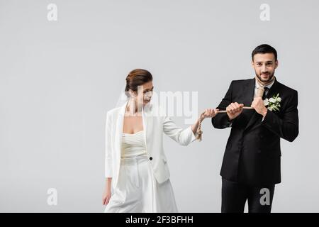 Mariée souriante tirant la corde autour du cou de l'arabe petit ami isolé en gris Banque D'Images