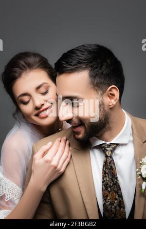 mariée heureuse avec les yeux fermés embrassant groom musulman heureux isolé en gris Banque D'Images