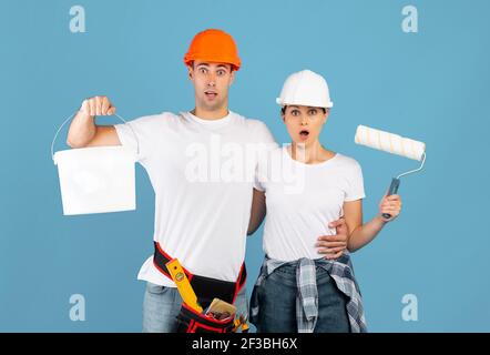 Portrait d'un couple choqué avec des outils de peinture dans les mains arrière-plan bleu Banque D'Images