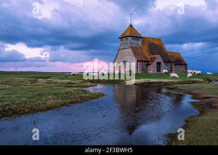 Église Saint Thomas Becket près de Fairfield sur le marais Romney dans le Kent, au sud-est de l'Angleterre, nuages de tempête se rassemblant pendant l'heure bleue et pâturage des moutons Banque D'Images