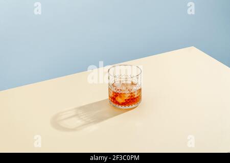 Verre avec Whiskey et Ice Cube sur table sur fond bleu. Style isométrique moderne. Concept créatif. Banque D'Images