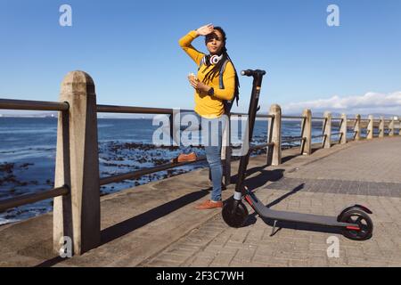 Femme afro-américaine ombragée par un sandwich au soleil sur la promenade par la mer Banque D'Images