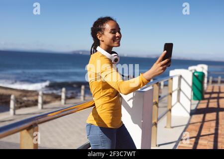 Femme afro-américaine souriante prenant le selfie avec un smartphone près du mer Banque D'Images