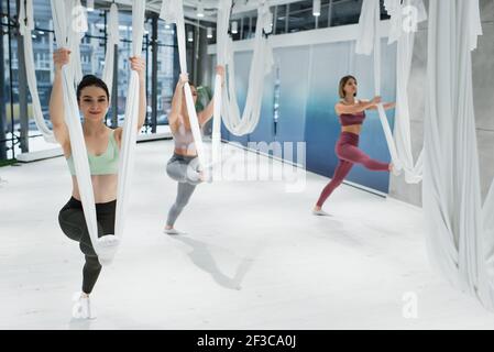 les jeunes femmes sportives s'échauffent avec des hamacs de yoga à la mouche dedans salle de sport Banque D'Images