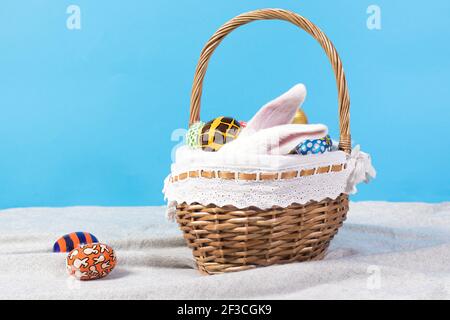 Longues oreilles blanches d'un vrai lapin moelleux dans un panier sur fond bleu avec des œufs de Pâques. Photo des fêtes de Pâques pour carte postale pour copier l'espace pour bannière. Banque D'Images