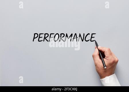 Main masculine écrivant le mot performance sur fond gris. Évaluer le concept de performance professionnelle, professionnelle ou commerciale. Banque D'Images