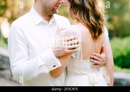 La mariée et le marié embrassent dans le parc, le marié met ses mains sur le dos de la mariée Banque D'Images