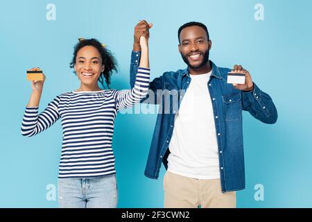 un couple afro-américain heureux tient la main tout en montrant des cartes de crédit sur bleu Banque D'Images