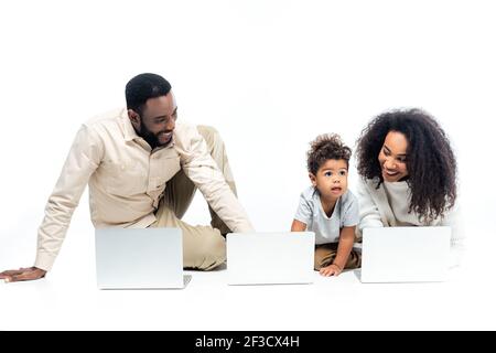 enfant afro-américain émerveillé à proximité de parents heureux et ordinateurs portables sur blanc Banque D'Images