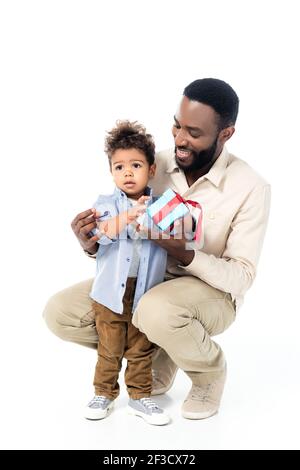 petit enfant afro-américain tenant présent près de père joyeux sur blanc Banque D'Images