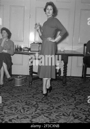 1957, historique, jeune femme elegenat dans une robe élégante de l'époque lors d'une fête de bureau dans un salon tenant un verre de vin, Victoria Hotel, Leeds, Angleterre. ROYAUME-UNI. Banque D'Images