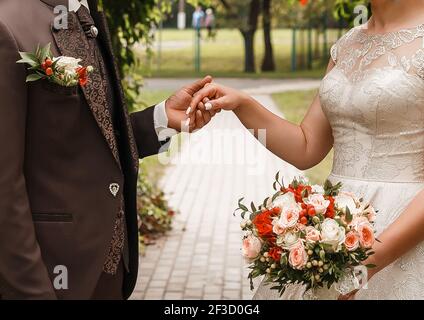 Le marié dans un costume brun tient la main de la mariée avec un bouquet de mariage. Banque D'Images