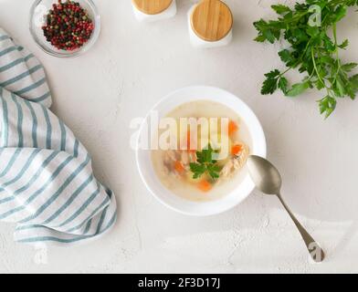 Soupe de poisson claire avec morceaux de légumes et de saumon dans un bol blanc sur une assiette blanche. Concept d'alimentation saine. Vue de dessus. Orientation horizontale. Banque D'Images