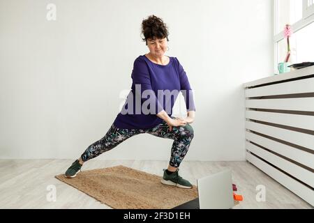 femme adulte en vêtements de sport faisant des exercices d'étirement et souriant tout en se tenant contre le mur gris. Une vie saine. Concept sport. Perte de poids. Banque D'Images