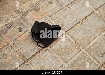 Image d'un masque noir non réutilisable qui protège contre la contagion De maladies respiratoires a chuté sur le terrain dans un européen ville Banque D'Images