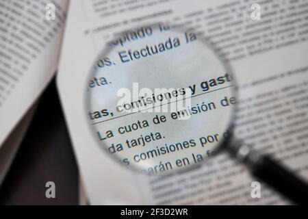 Une loupe indique sur un papier les mots dans les commissions, frais et dépenses espagnols dans un document de banque Banque D'Images