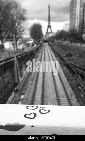 Romantisme urbain parisien. Cœurs sur la balustrade du pont avec vue sur le chemin de fer et la tour Eiffel en arrière-plan. Photo historique noir blanc. Banque D'Images