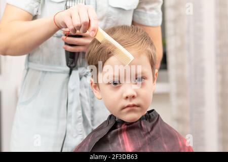 jeune maman coiffeur coupe son bébé garçon à la maison avec une tondeuse à cheveux pendant la quarantaine. foyer sélectif. portrait Banque D'Images