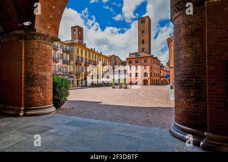 Vue sur la place de la ville pavée parmi les maisons anciennes et les tours médiévales sous un beau ciel à Alba, Piémont, Italie du Nord. Banque D'Images