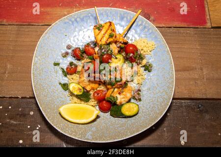 Une délicieuse assiette de saumon de printemps et de brochettes de crevettes avec salade de couscous et salsa aux agrumes sur une table de cuisine en bois Banque D'Images